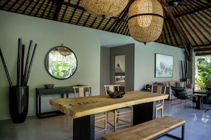 A modern dining area with a wooden table, benches, and a round mirror on the wall. - The Amala Boutique Retreat (Seminyak)