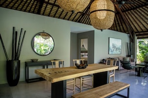 Uma área de jantar moderna com mesa de madeira, bancos e um espelho redondo na parede.