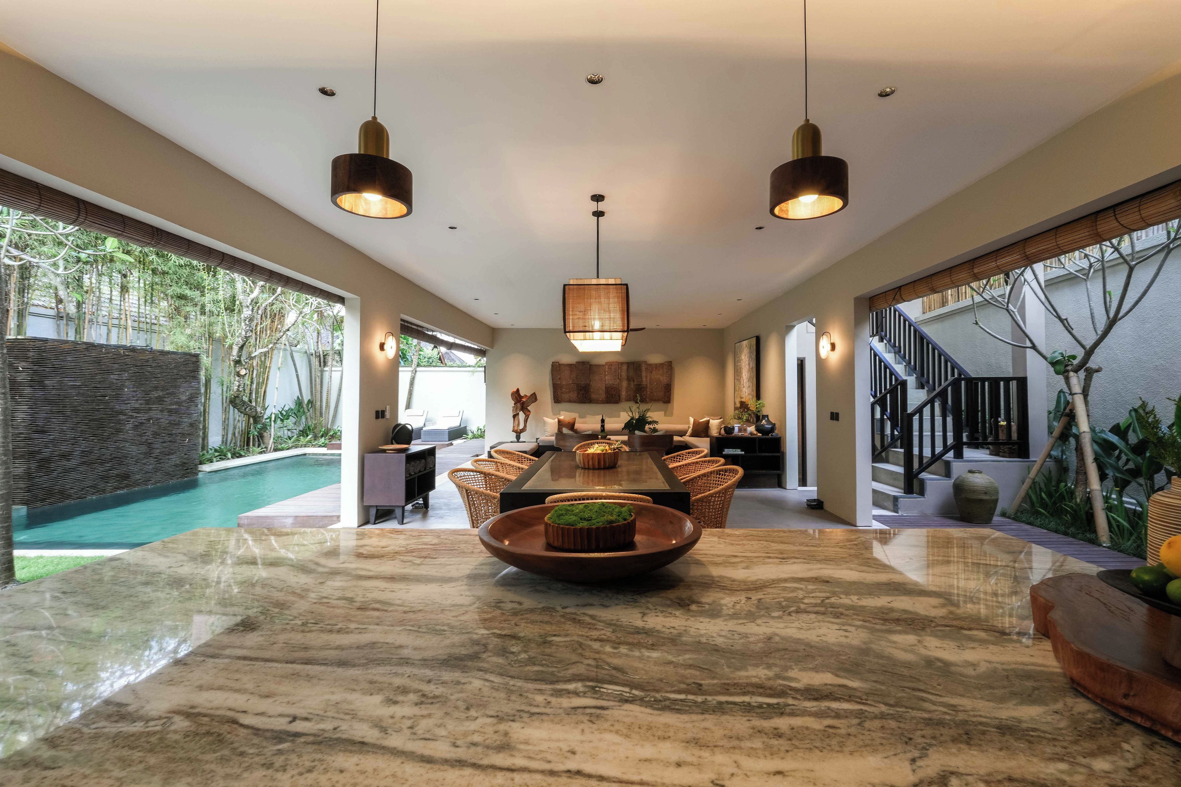 A spacious dining area with a marble table, surrounded by wicker chairs, and a view of a swimming pool.