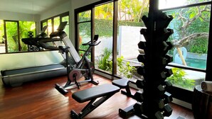 A home gym with exercise equipment, large windows, and a view of greenery. - The Amala Boutique Retreat (Seminyak)