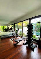 A home gym with exercise equipment, large windows, and a view of greenery.