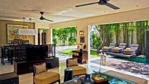 Un vaste espace de vie doté d’un téléviseur à écran plat, de sièges confortables, d’une table basse et offrant une vue sur un jardin luxuriant ainsi que sur un espace de détente extérieur.