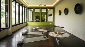 Sala de yoga com tapetes, almofadas, ponto de água e espelho.