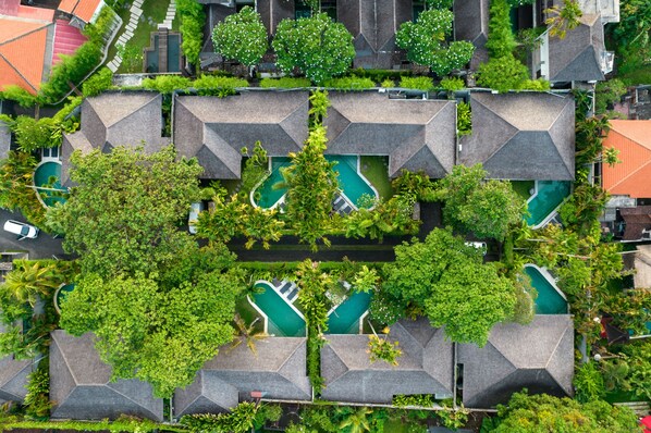 An aerial view of a resort with multiple swimming pools surrounded by lush greenery and modern architecture. - The Amala Boutique Retreat (Seminyak)
