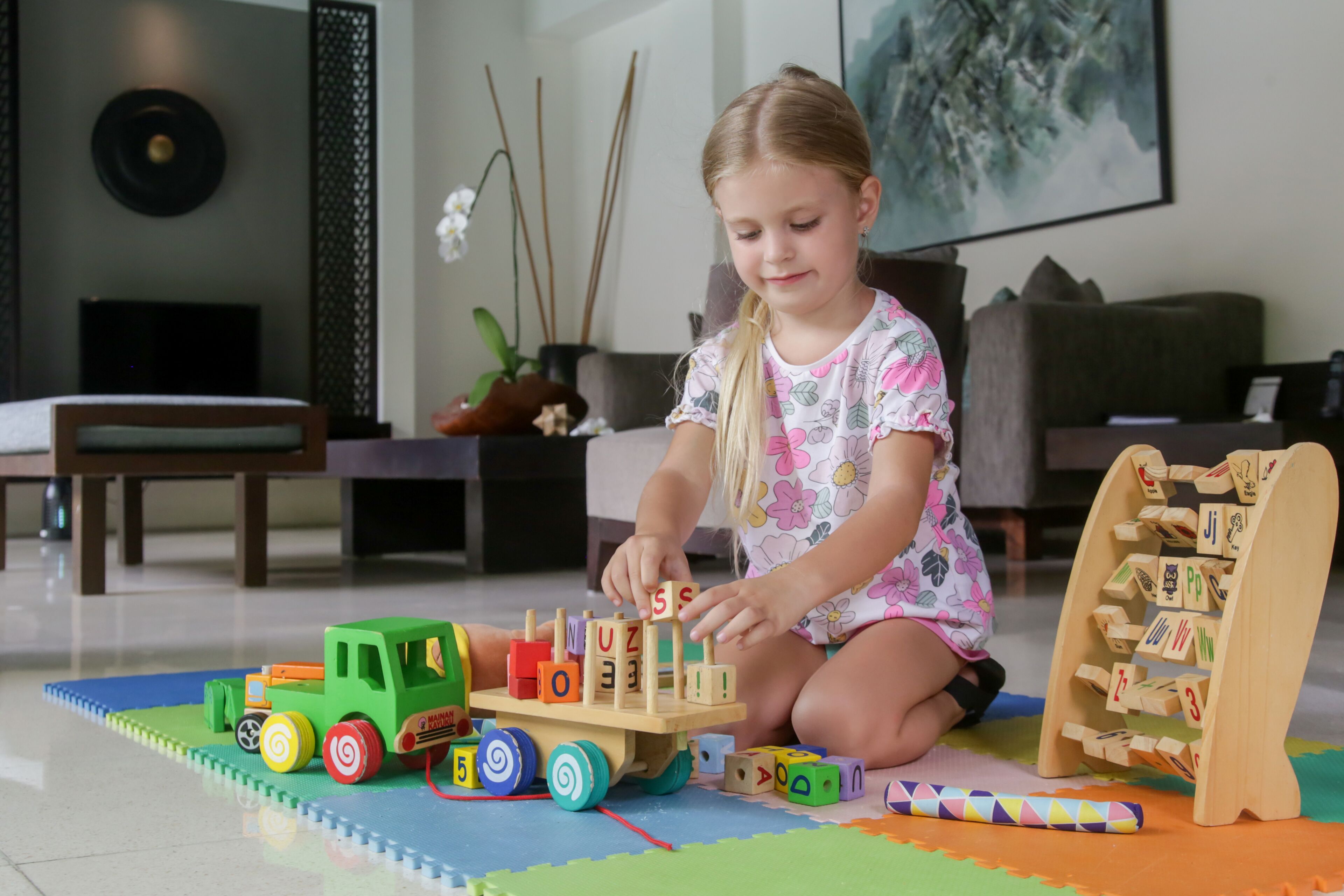 Een kind speelt met houten blokken en een speelgoedtruck op een kleurrijke speelmat.