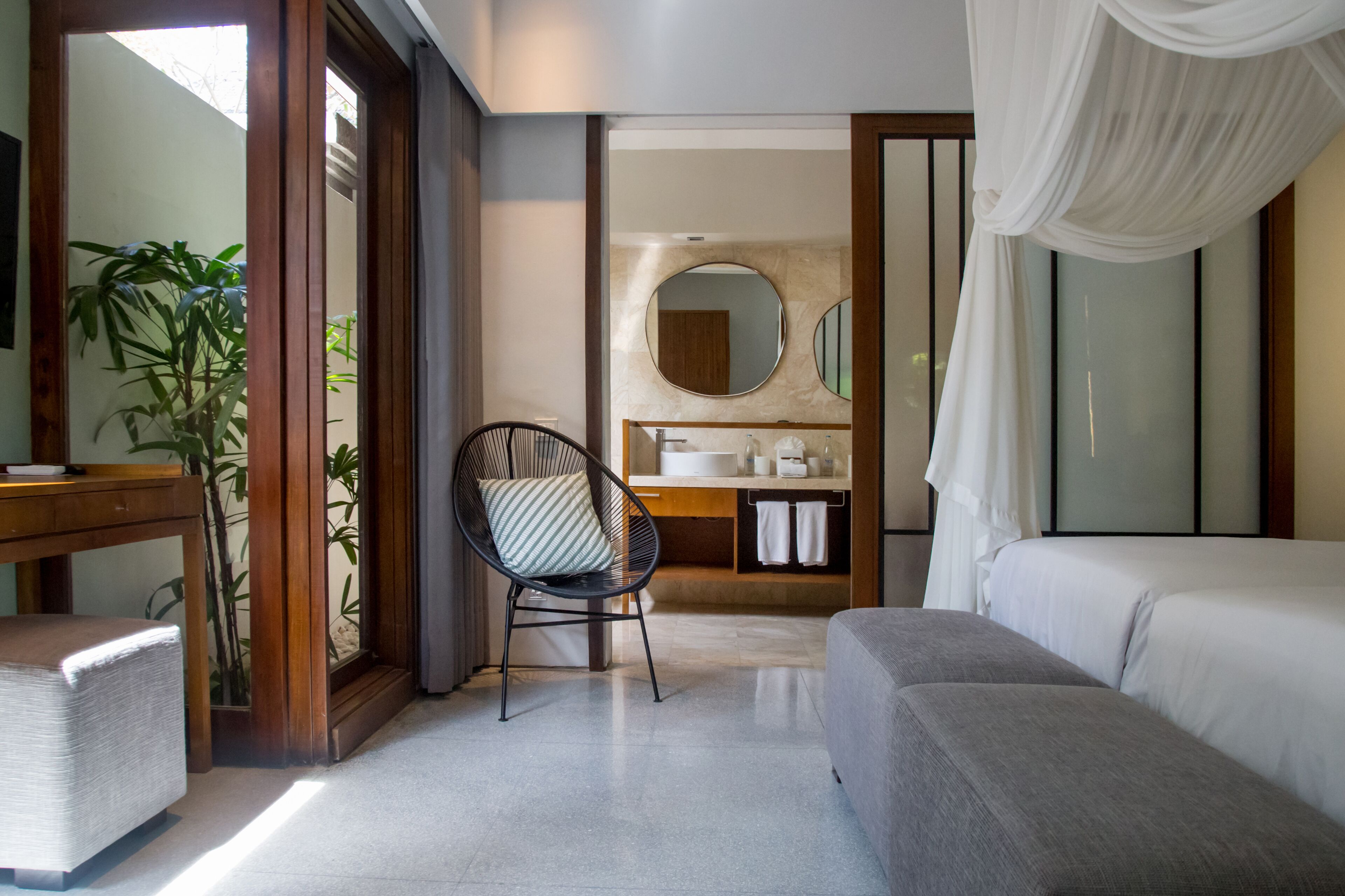A modern bedroom with a large bed, a chair, a desk, and a bathroom visible through an open door.