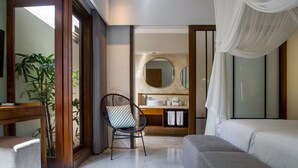 A modern bedroom with a large bed, a chair, a desk, and a bathroom visible through an open door. - The Amala Boutique Retreat (Seminyak)