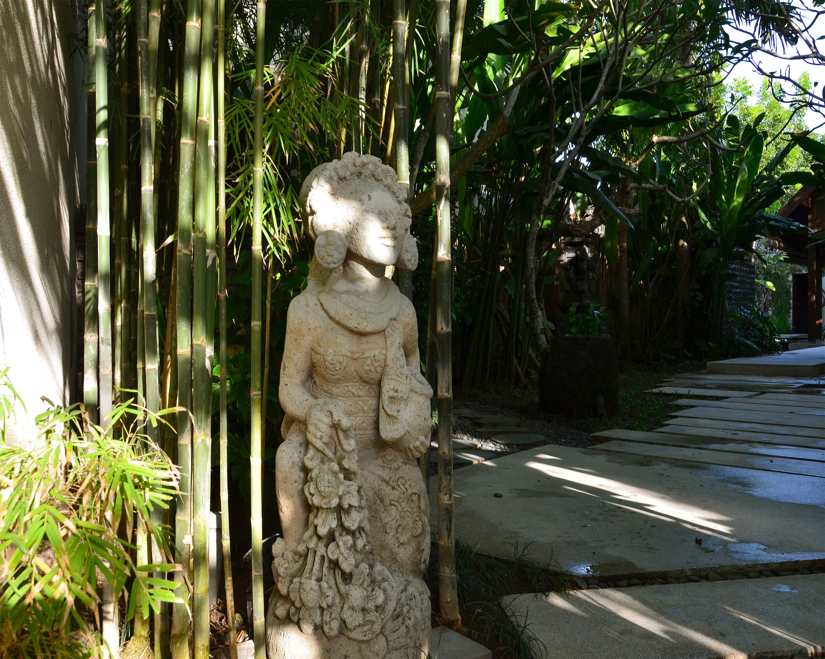 A stone statue in a garden with bamboo and other greenery.