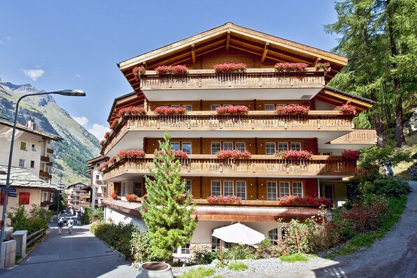 A multi-story wooden building with balconies adorned with red flowers, set against a mountainous backdrop. - Hotel Albatros Zermatt (Zermatt)