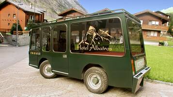 A green bus with "Hotel Albatros" written on the side parked on a paved area with buildings and a mountain in the background.