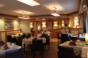 A hotel dining area with multiple tables and chairs, wooden paneling, and pendant lighting. - Hotel Albatros Zermatt (Zermatt)