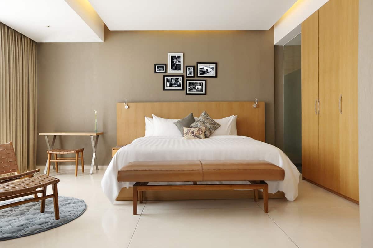 Un dormitorio moderno con una cama grande, cabecera de madera, un banco, un escritorio y un armario.