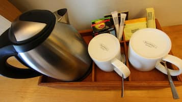 Una bandeja con una tetera de acero inoxidable, dos tazas blancas Royal White, una cuchara y algunos alimentos envasados.