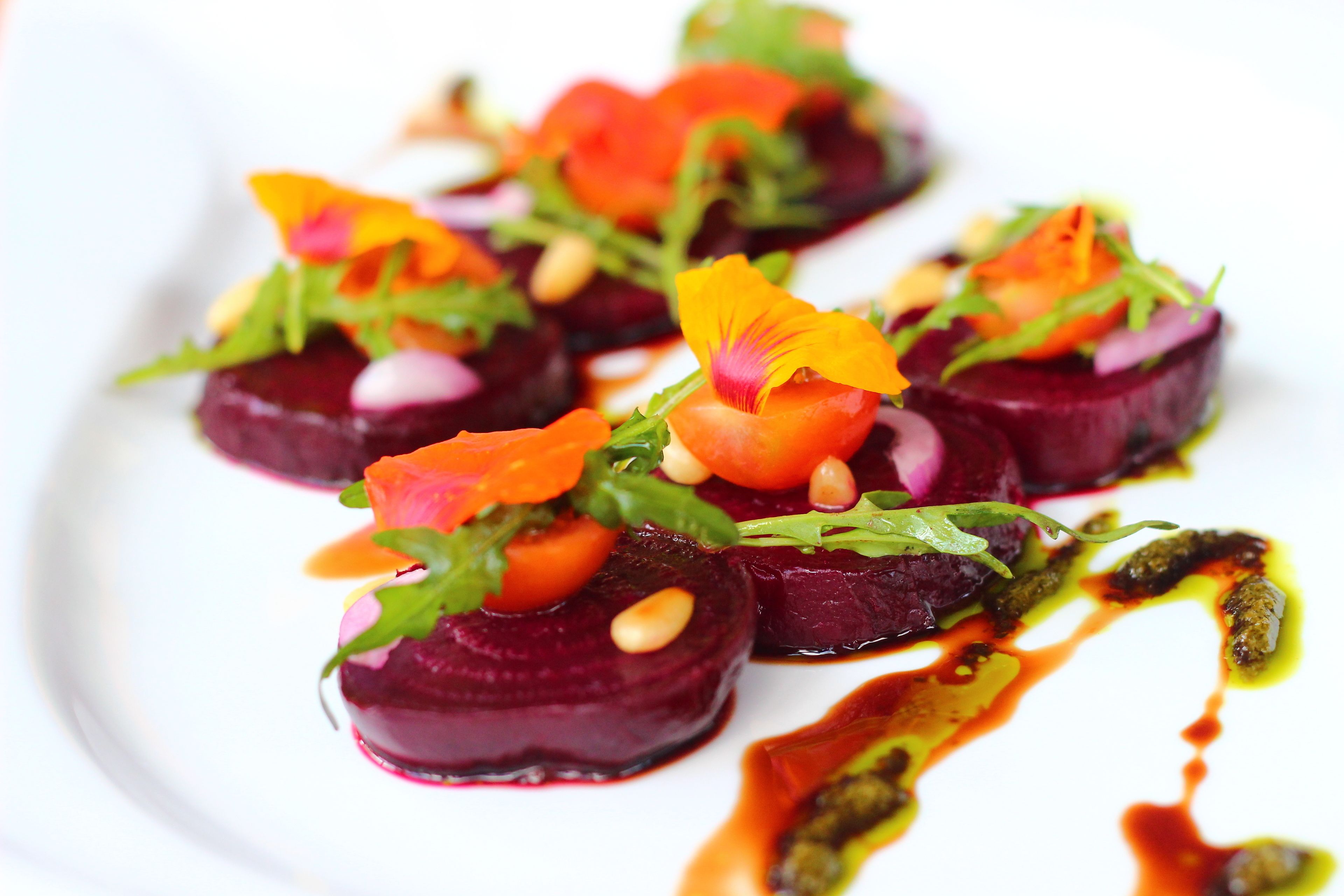 A plate of food with beetroot slices, greens, and orange flowers.