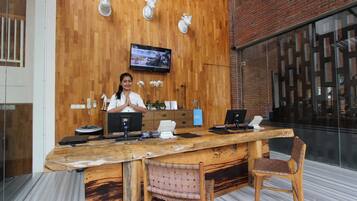 A wooden reception desk with a television, a laptop, and a phone. There are two chairs and a plant on the desk.