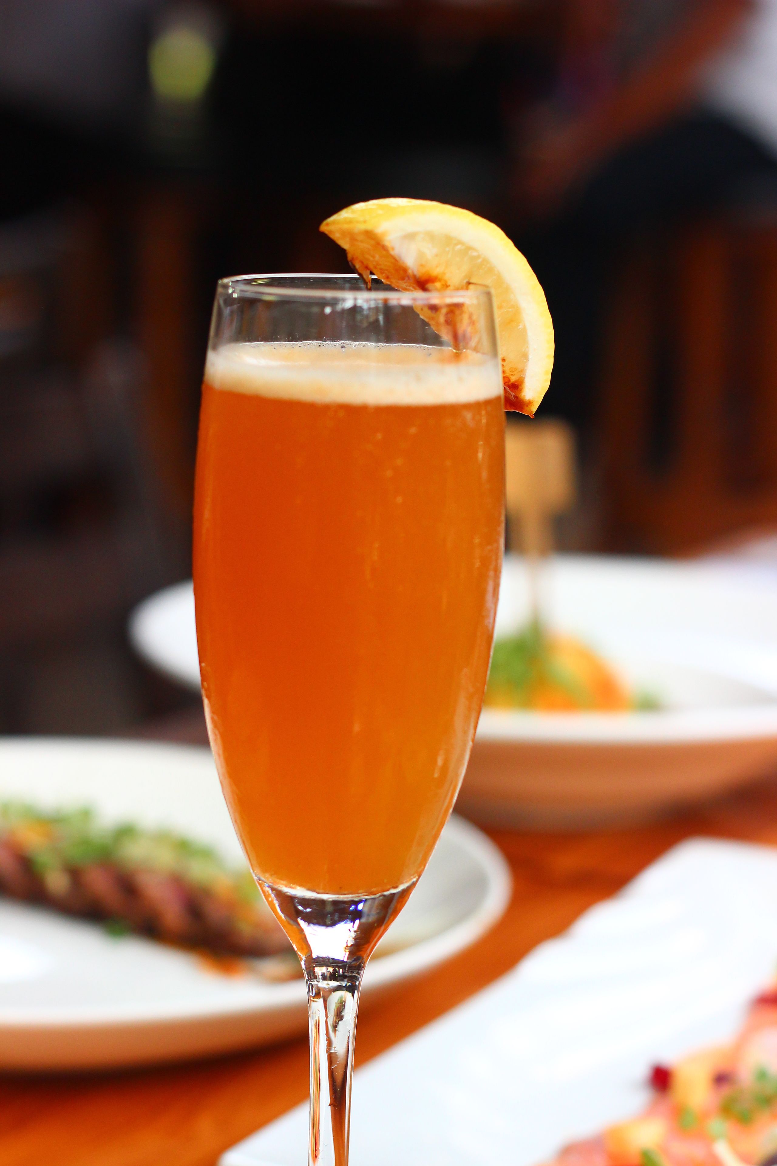 A tall glass of beer with a lemon slice garnish on a wooden table.