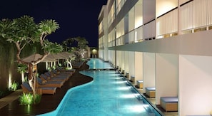 A swimming pool with lounge chairs and umbrellas, surrounded by a building with multiple floors. - Ossotel Legian Bali (Legian)