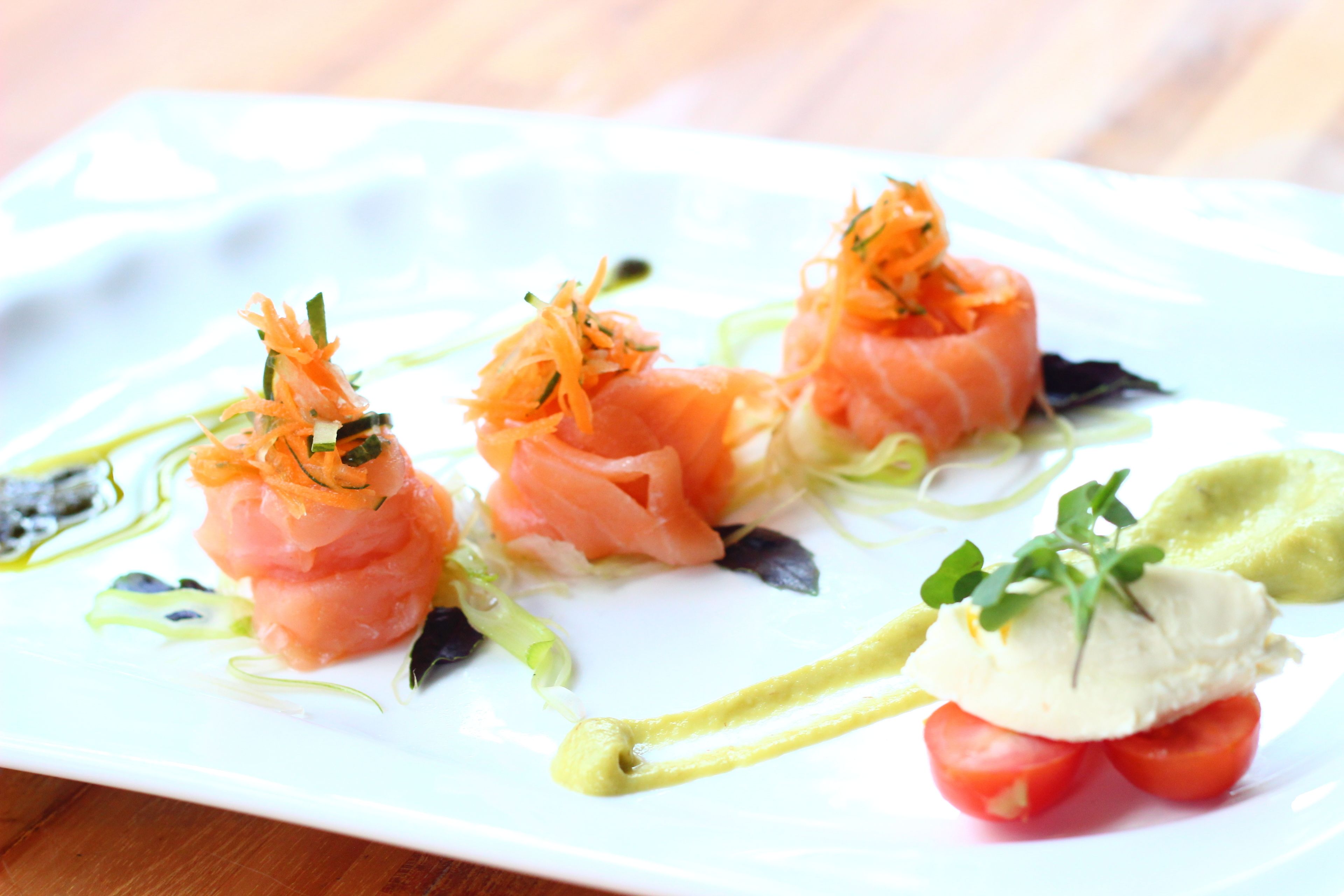 A white plate with food items including salmon, vegetables, and a dollop of sauce.