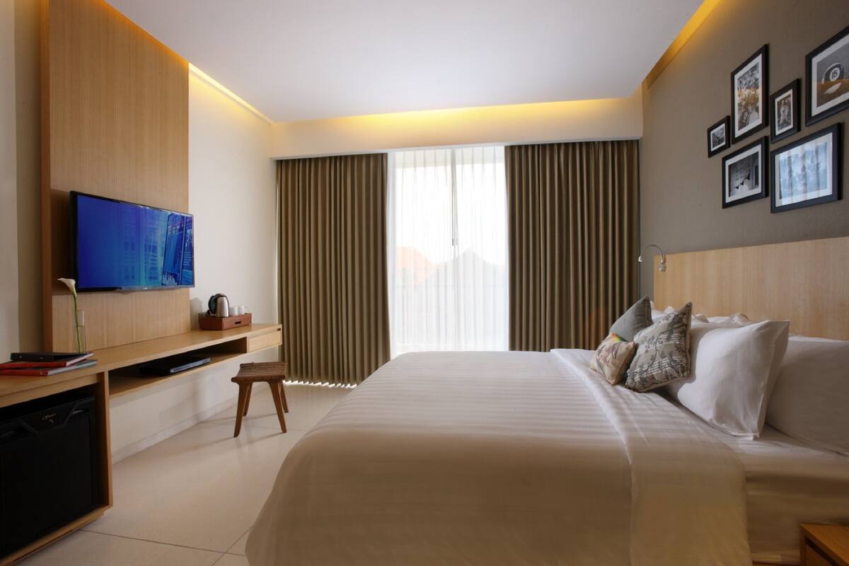 Una habitación de hotel con una cama grande, un televisor de pantalla plana montado en la pared, un escritorio con una silla y una ventana con cortinas.