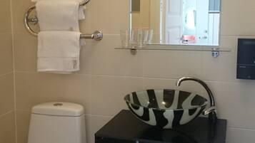 A bathroom with a toilet, a sink with a zebra-striped soap dish, a towel rack with multiple towels, a mirror, and a trash bin.