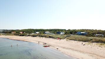 A beach with clear water, sandy shore, and houses in the background.