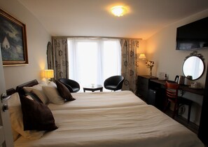 Une chambre d’hôtel avec deux lits, un bureau avec une chaise, une télévision et une fenêtre avec des rideaux.
