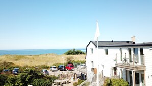 Un bâtiment situé sur la côte, doté d’un balcon donnant sur la mer, avec des voitures garées et un mur en pierre.