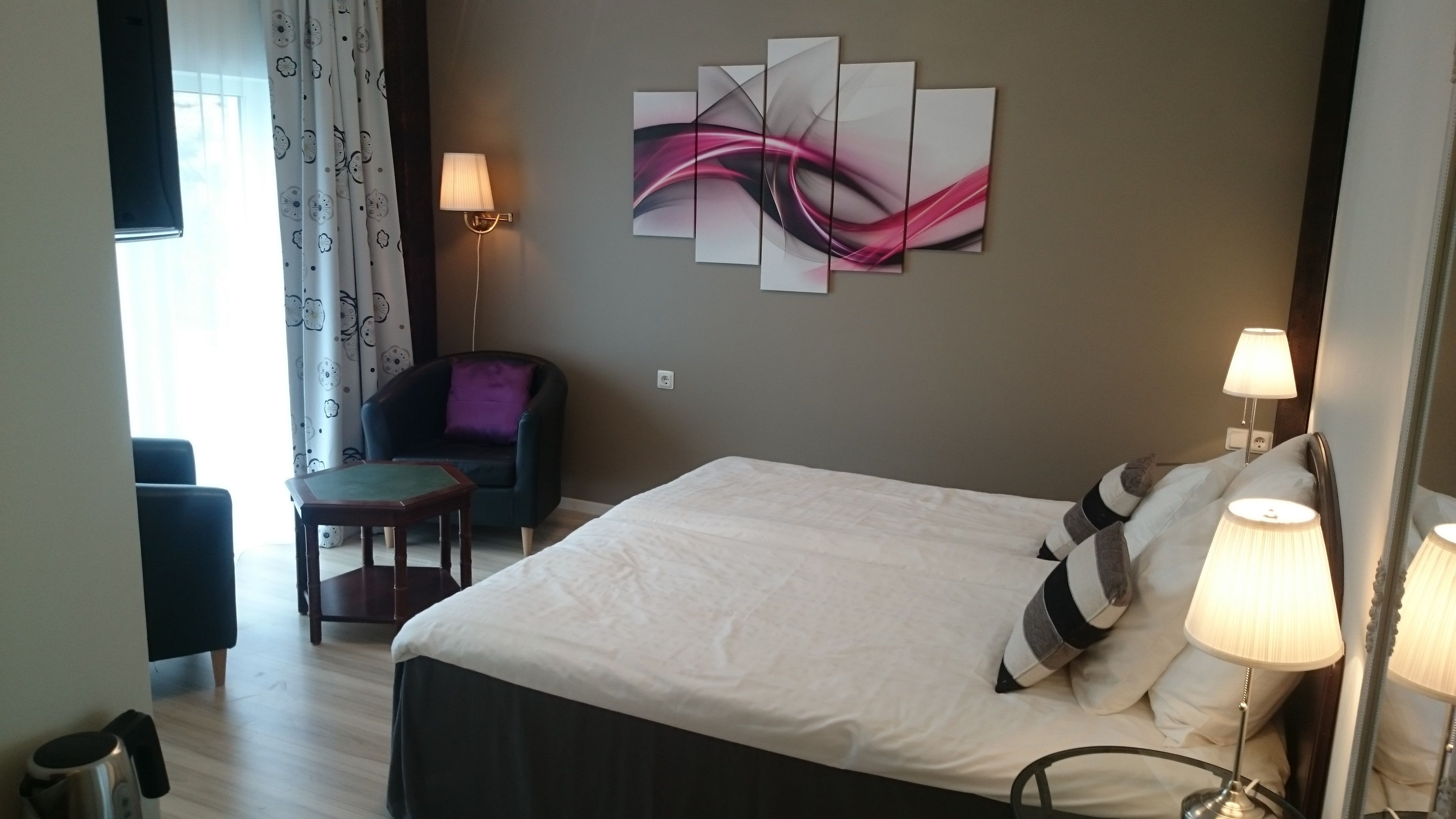 Ett hotellrum med en säng, en stol, ett bord och en vägglampa.