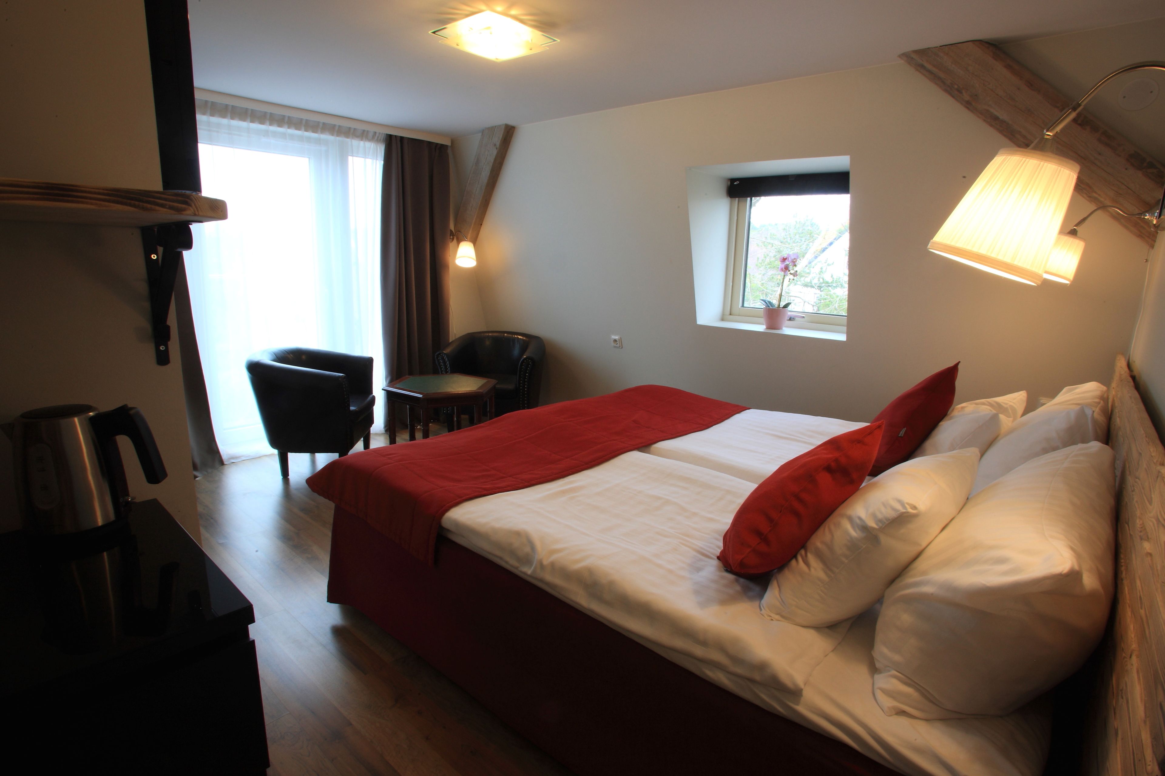 Una habitación de hotel con cama, una silla, una mesita, una ventana y una lámpara.