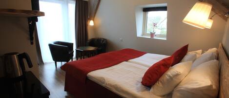 Una habitación de hotel con cama, una silla, una mesita, una ventana y una lámpara.