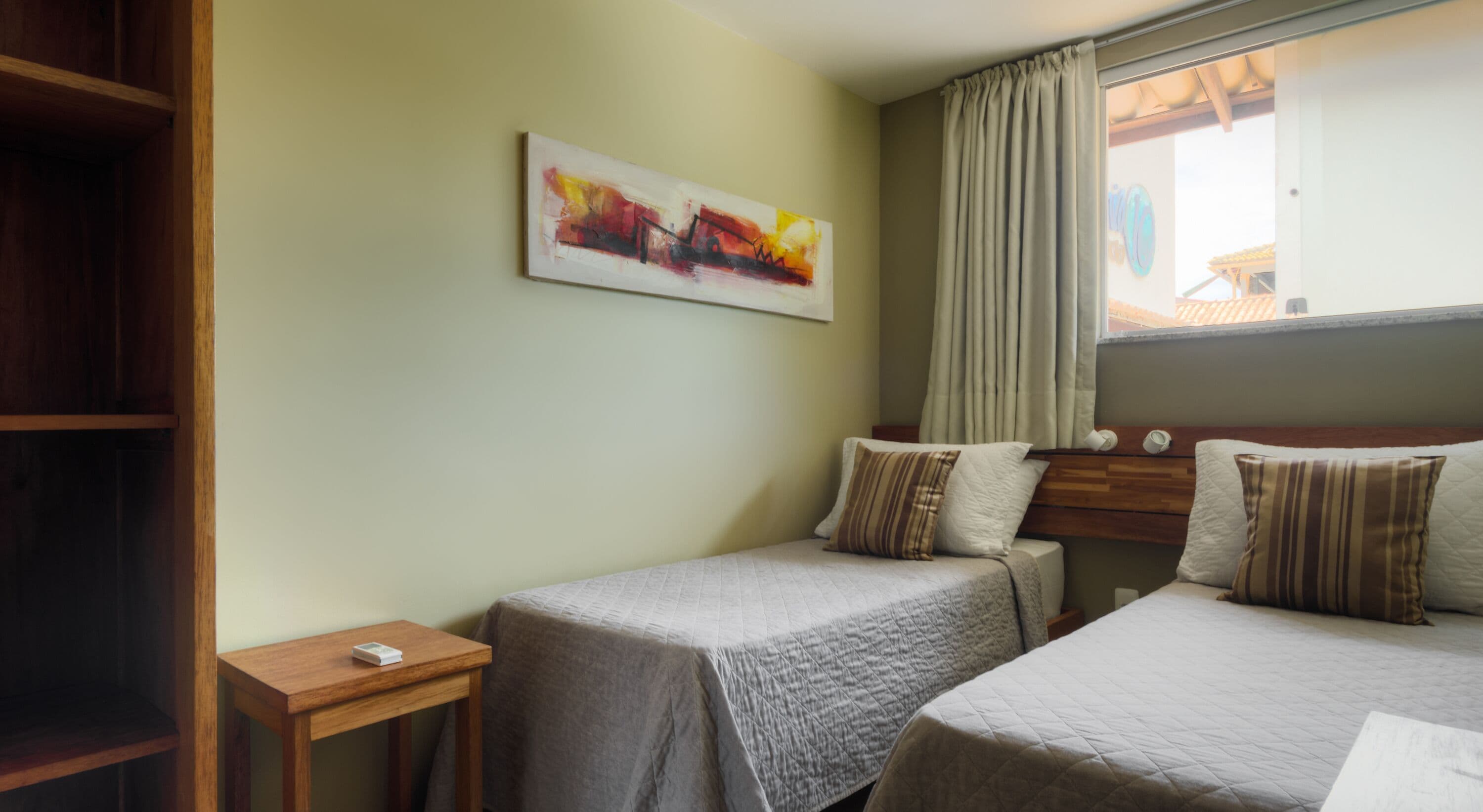 Een hotelkamer met twee bedden, een houten nachtkastje, een schilderij aan de muur en een raam met gordijnen.