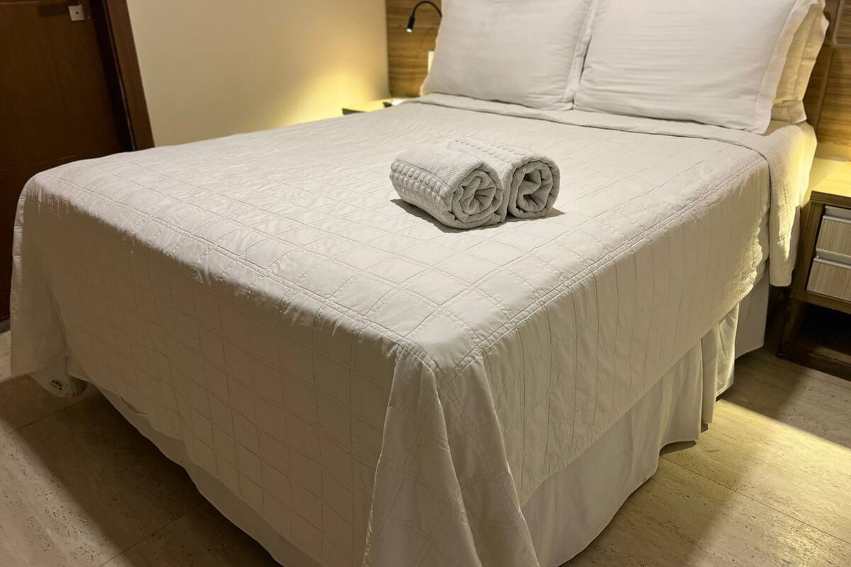 Un lit bien fait, avec une couvre-lit matelassé, deux oreillers et des serviettes enroulées posées sur le lit.