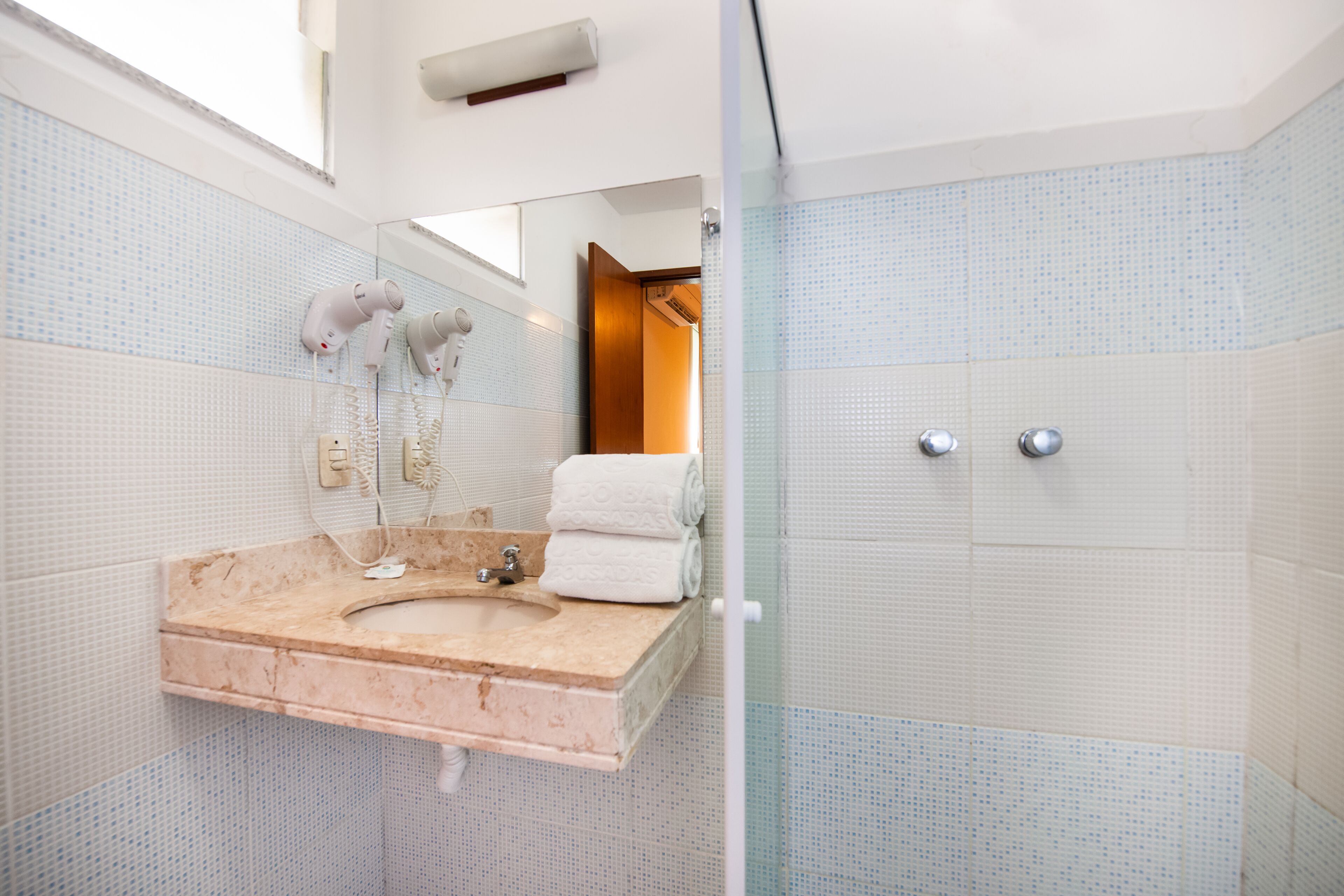A bathroom with a marble sink, a glass shower enclosure, and a tiled wall.