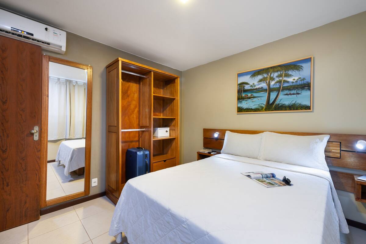 Une chambre d’hôtel avec un grand lit, une armoire, un bureau et un tableau représentant un paysage tropical.