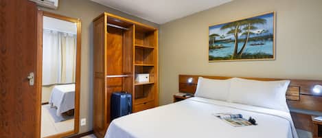 A hotel room with a large bed, a wardrobe, a desk, and a painting of a tropical scene.
