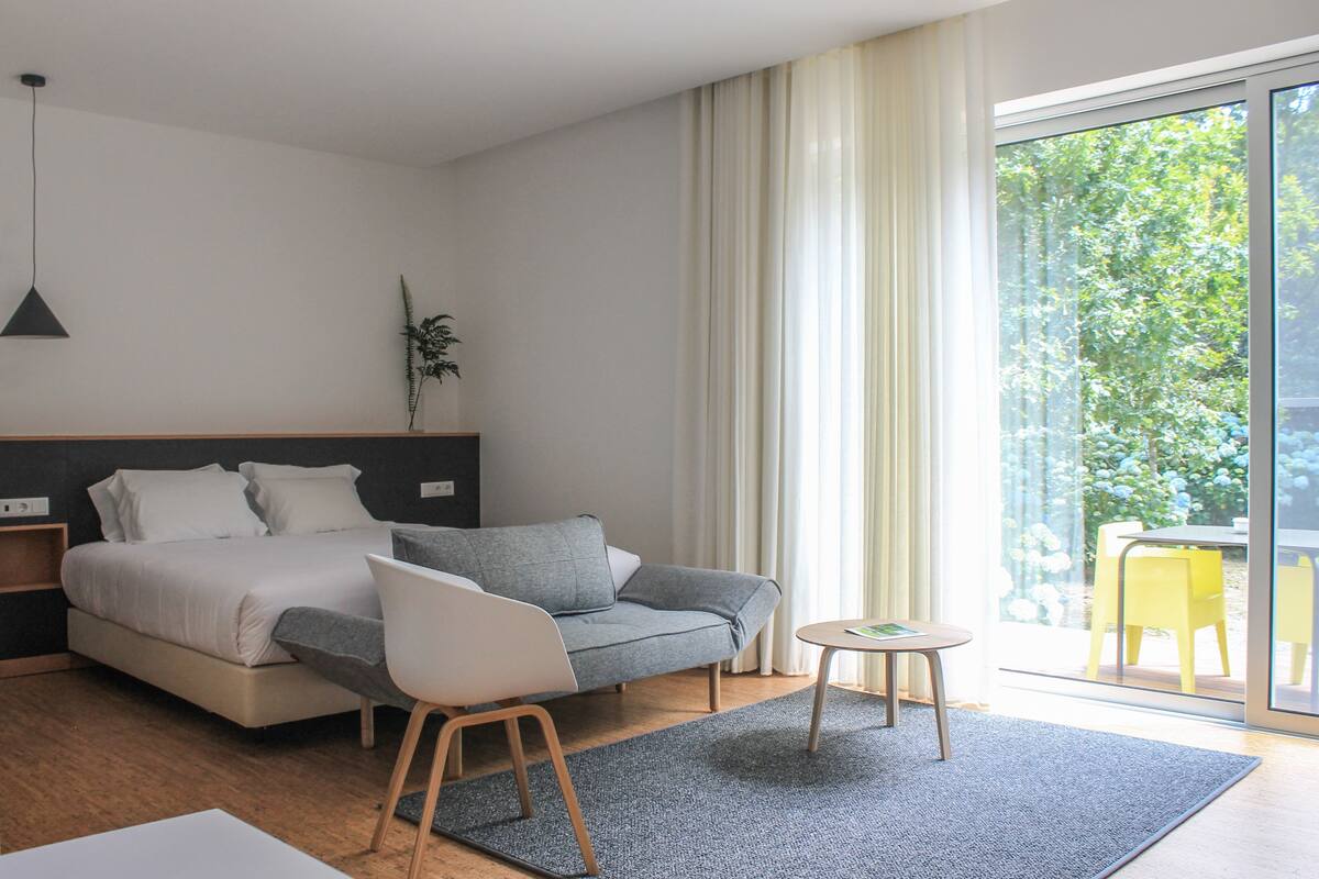 Een moderne slaapkamer met een bed, een grijze bank, een bijzettafeltje en een plant.