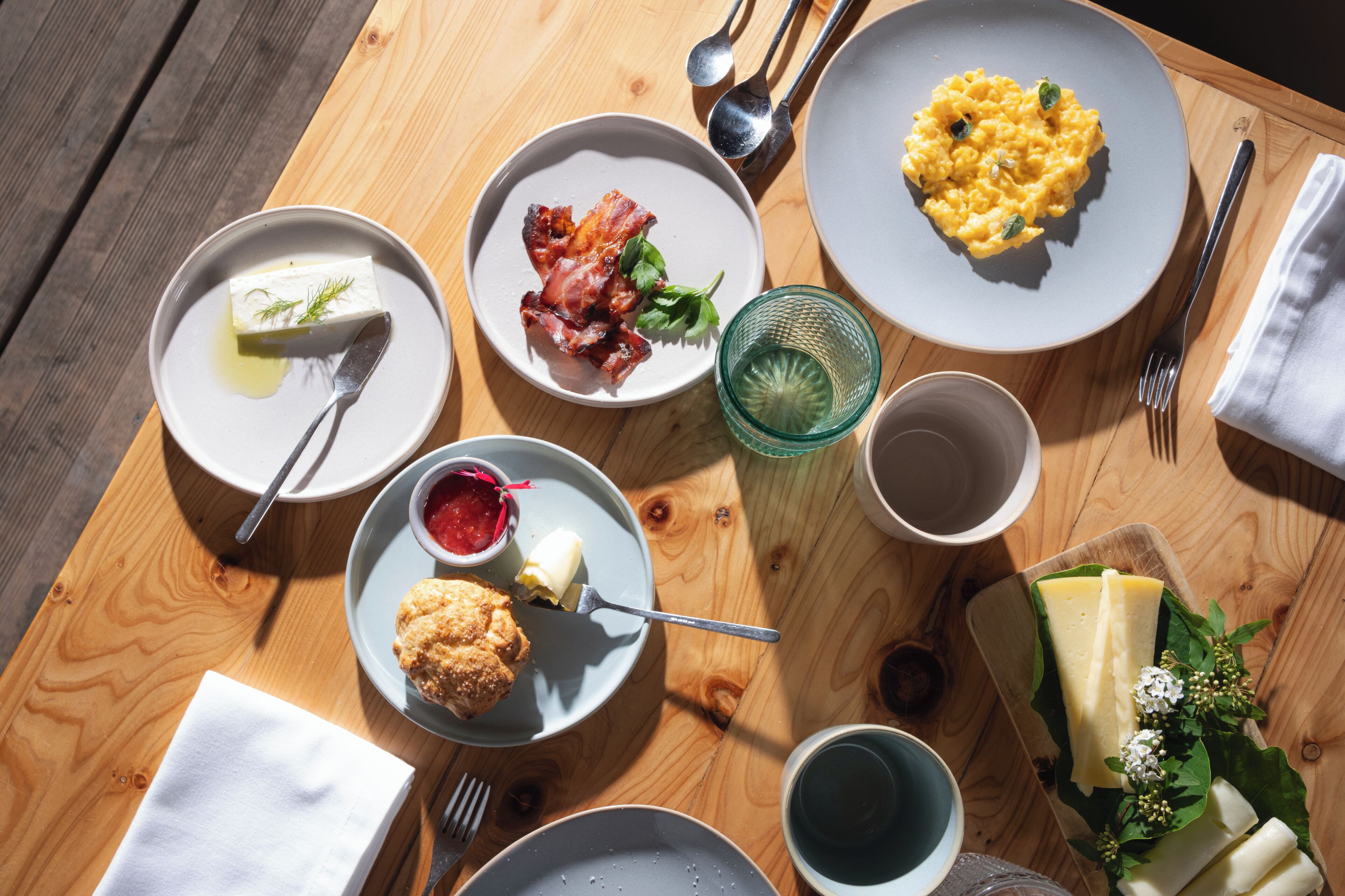 A wooden table with various breakfast items including eggs, bacon, butter, and a muffin.