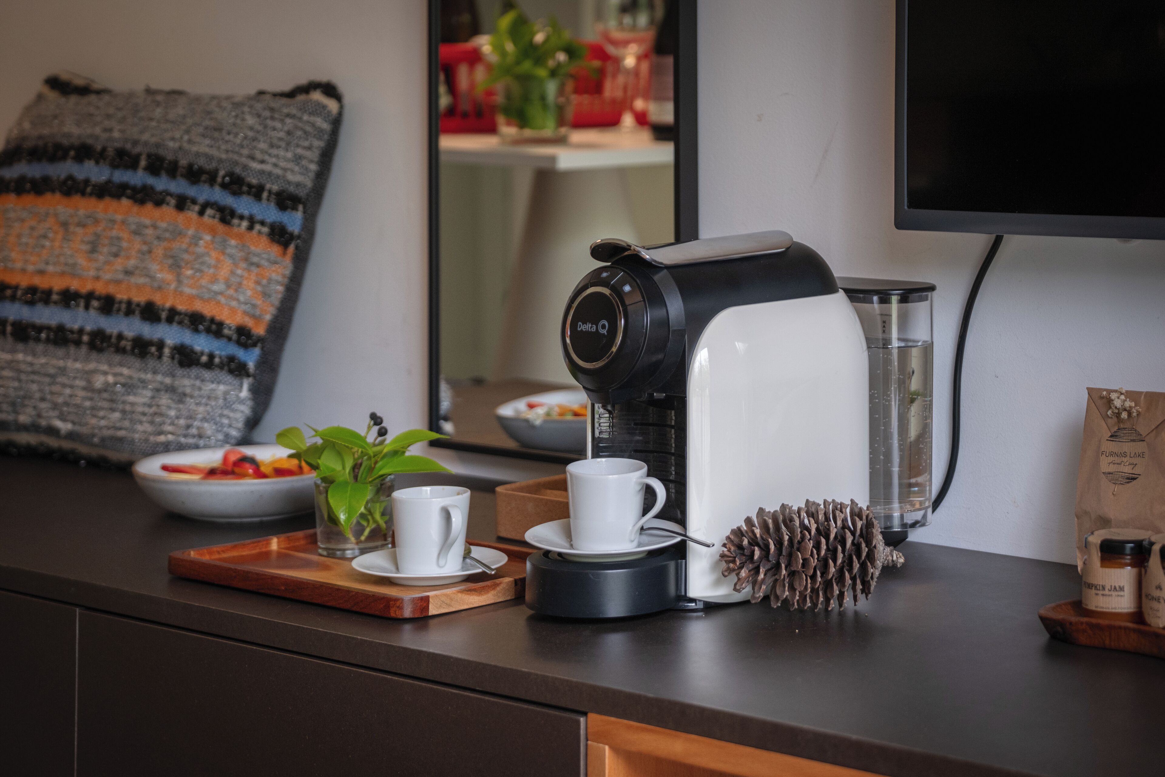 A coffee maker on a counter with a tray, a small plant, and a bowl of fruit.