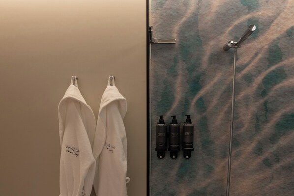 Un baño con dos toallas blancas colgadas en ganchos, una ducha con grifo metálico y tres botellas de productos Porten-Cale.