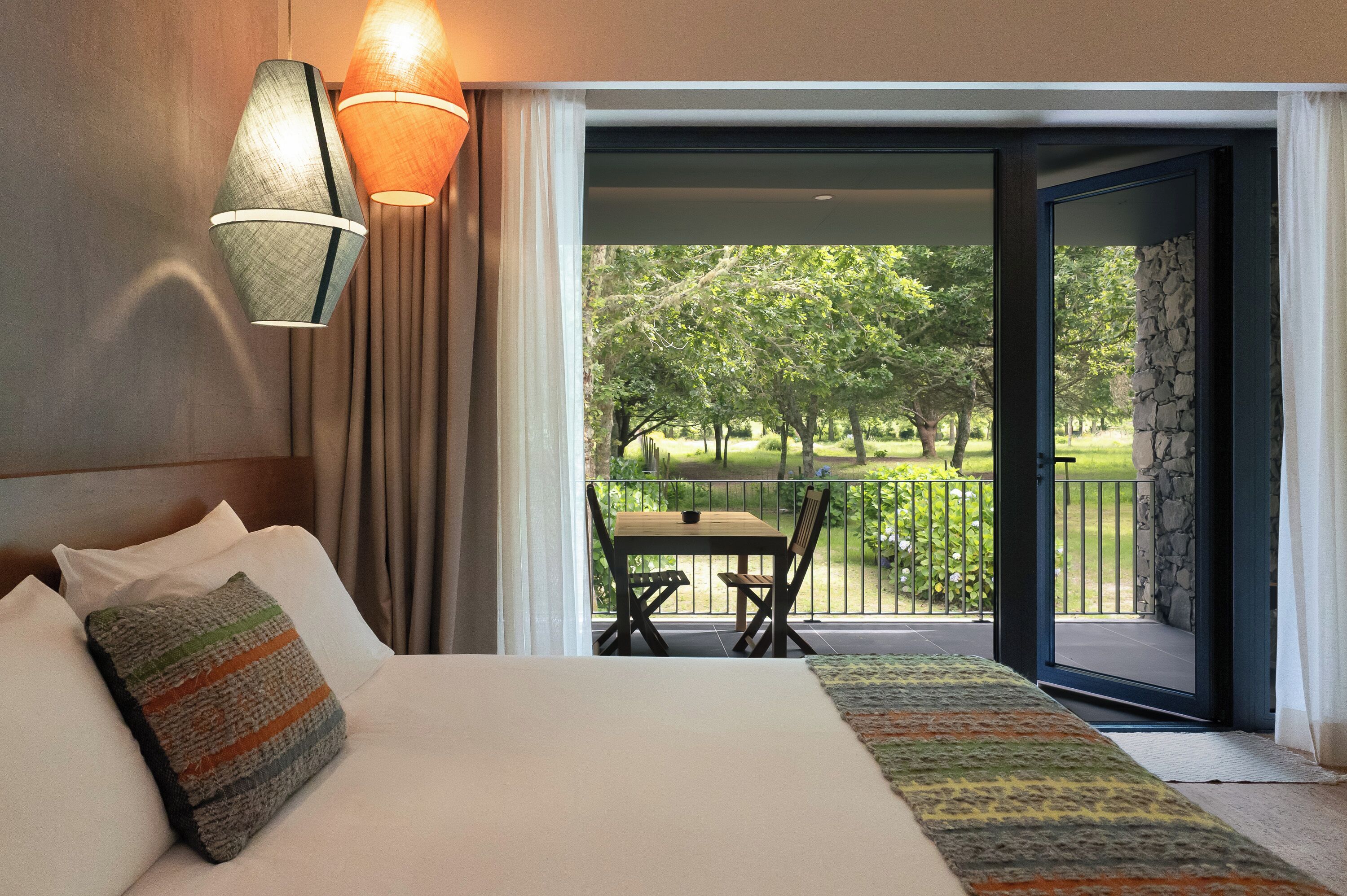 Ein Hotelzimmer mit einem Bett, Blick auf einen Balkon mit Tisch und Stühlen sowie einer zur Außenwelt führenden Tür.