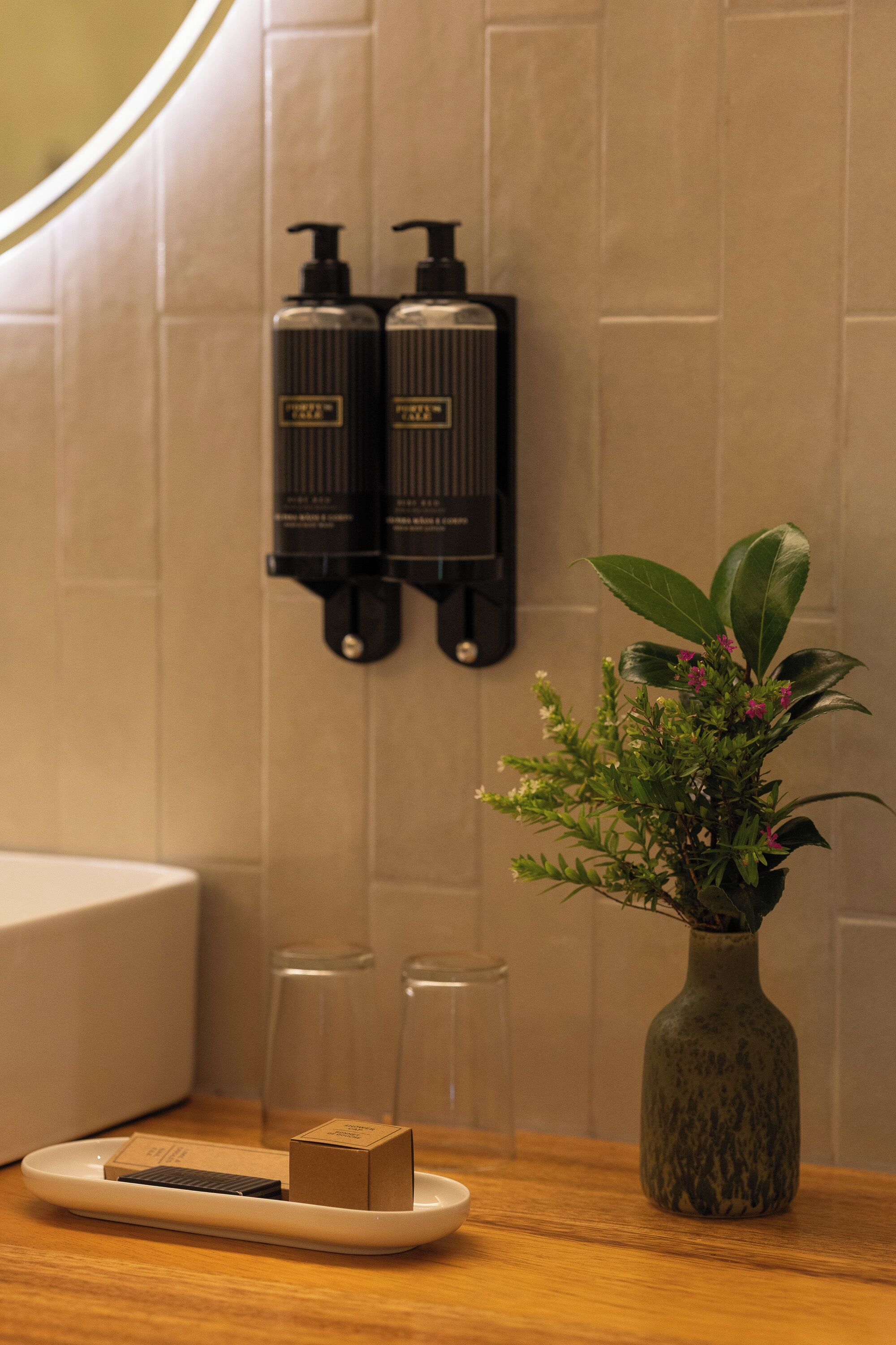 A bathroom with a wooden vanity, a small potted plant, two bottles of shampoo, and a soap dispenser.