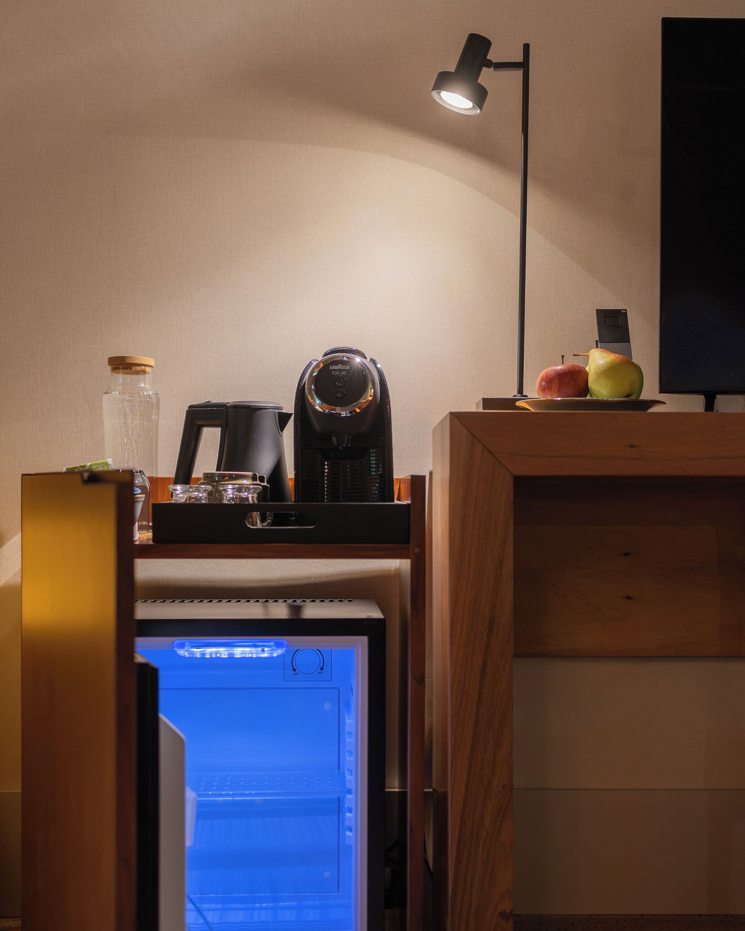 Ett köksutrymme med en kaffebryggare, en vattenkokare, en flaska och en fruktskål på bänken.