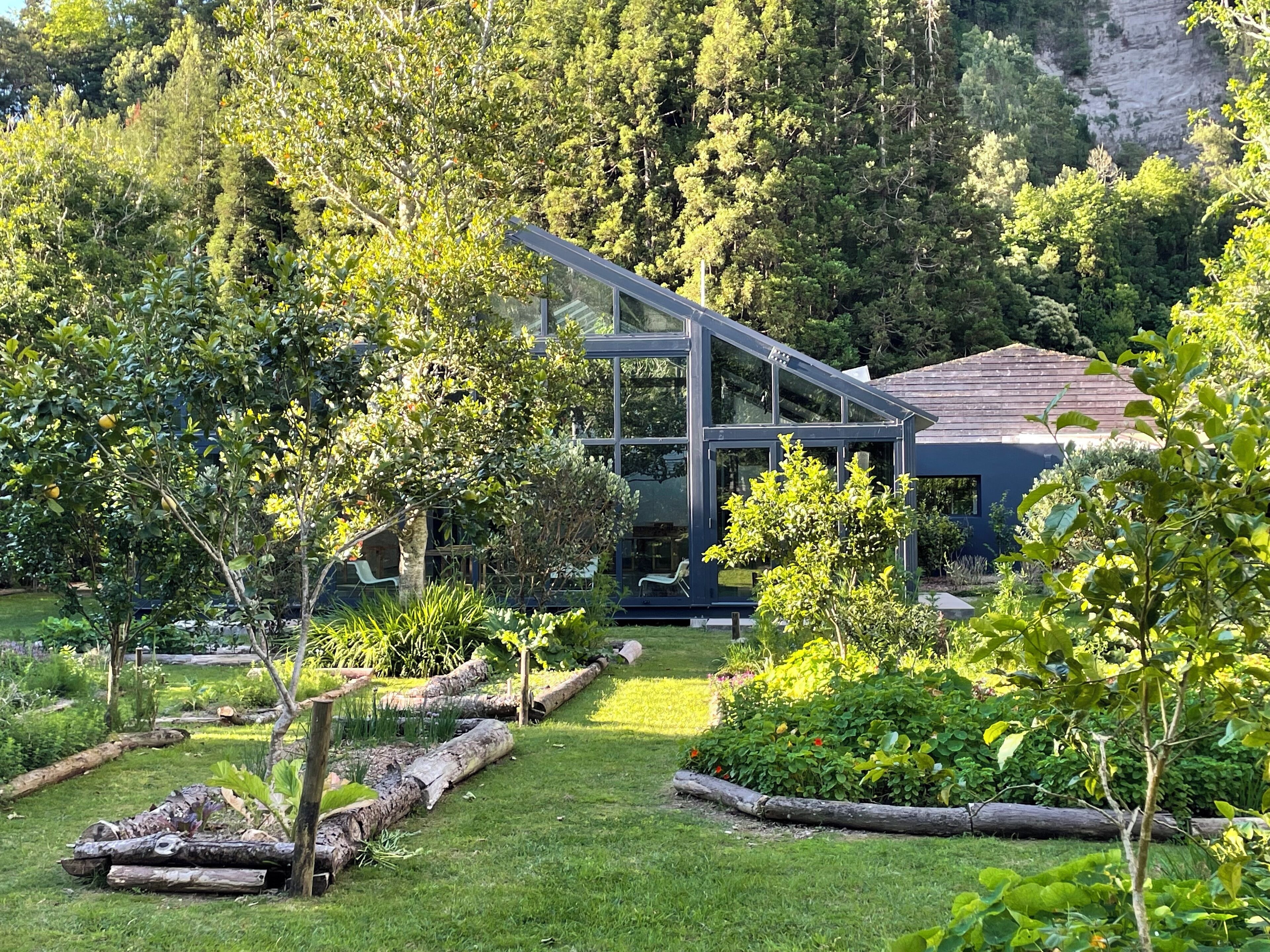 Une maison moderne dotée de grandes fenêtres en verre, entourée d’une végétation luxuriante et d’un jardin bien entretenu.