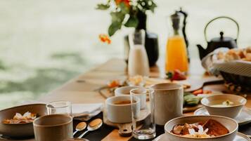 Uma mesa de café da manhã montada ao ar livre, com diversos pratos, copos e um vaso de flores.