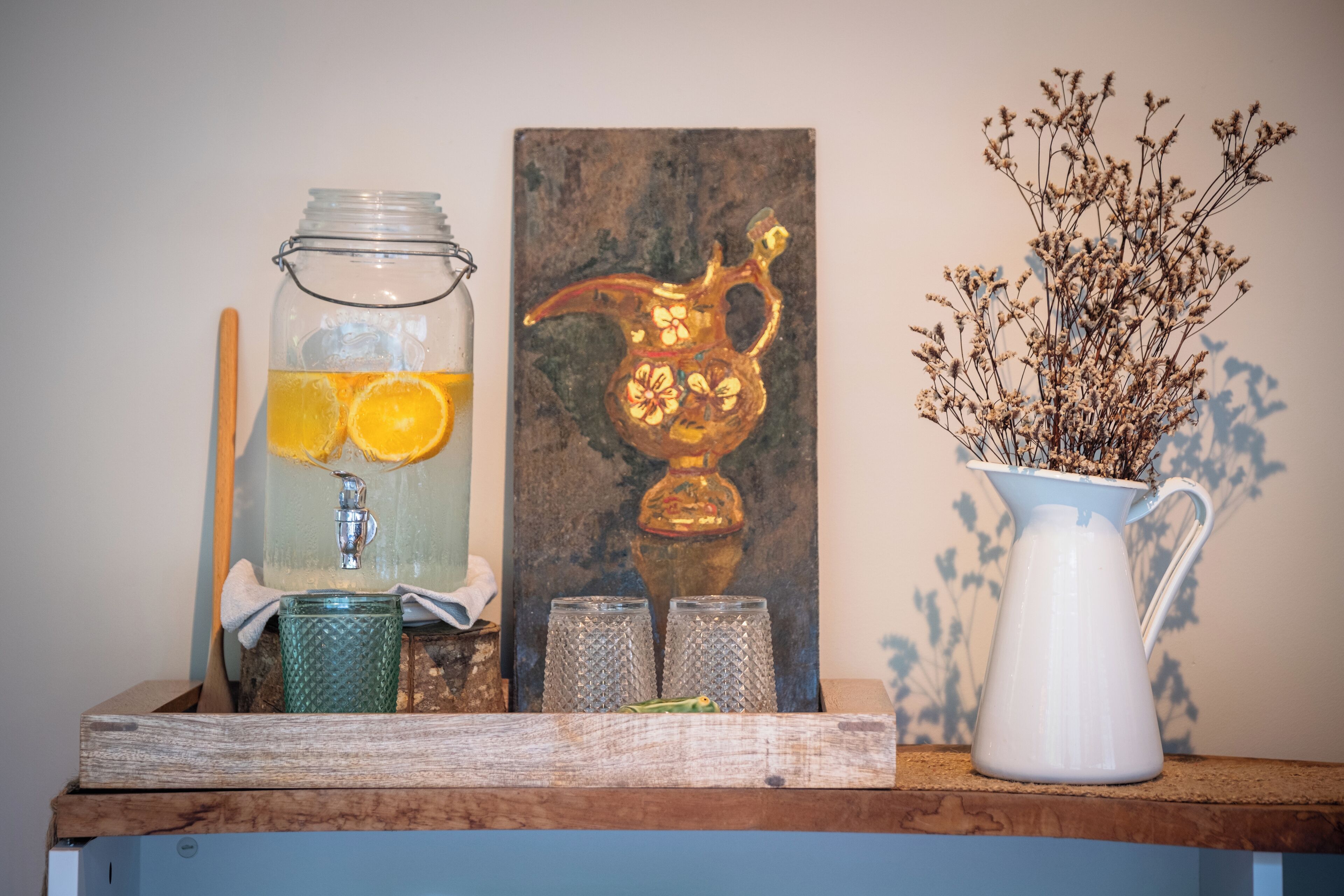 En hylde med et glas, en kande og en vase med tørrede blomster.
