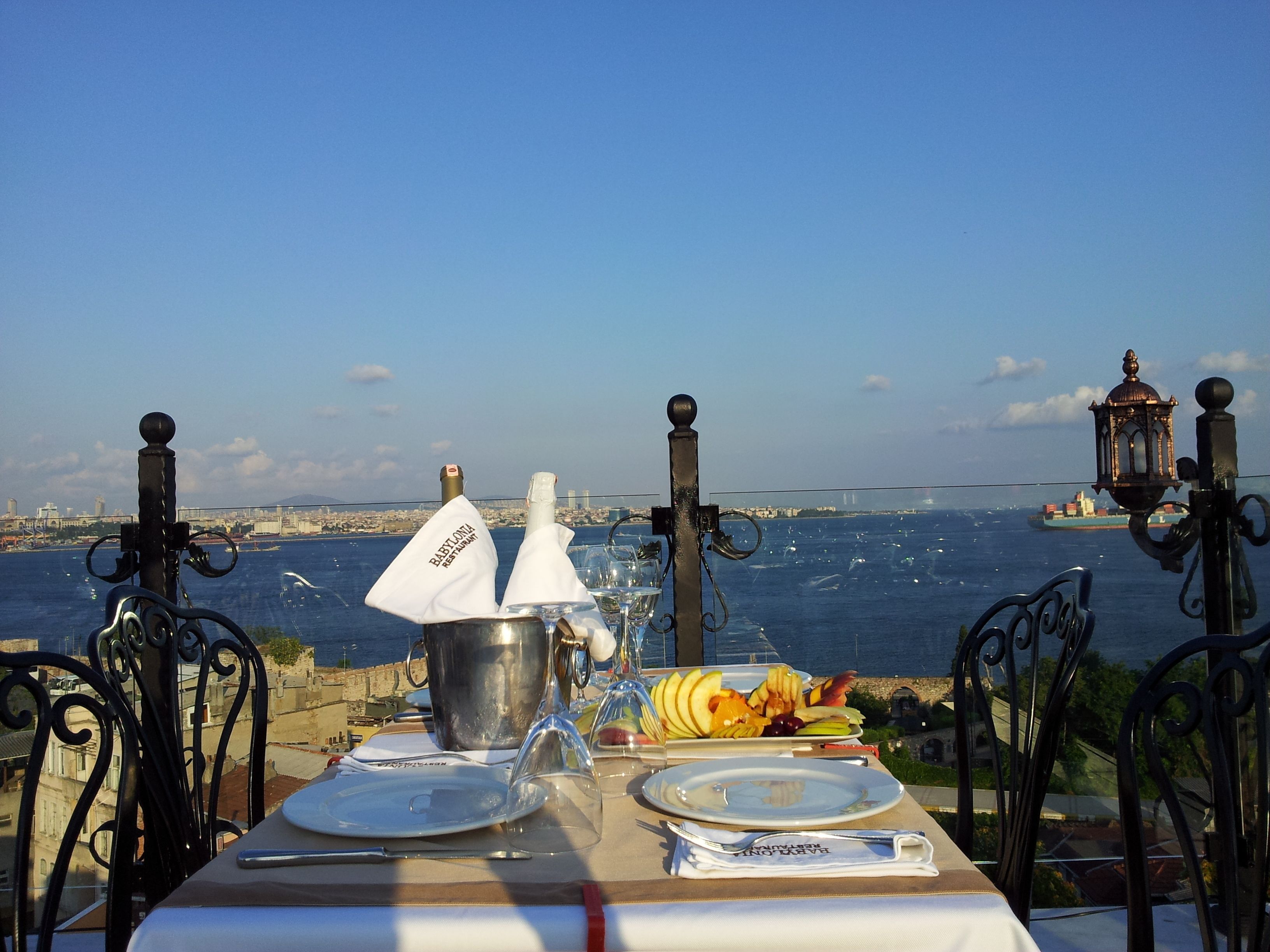 A table set for a meal with a view of the sea and a ship in the distance.