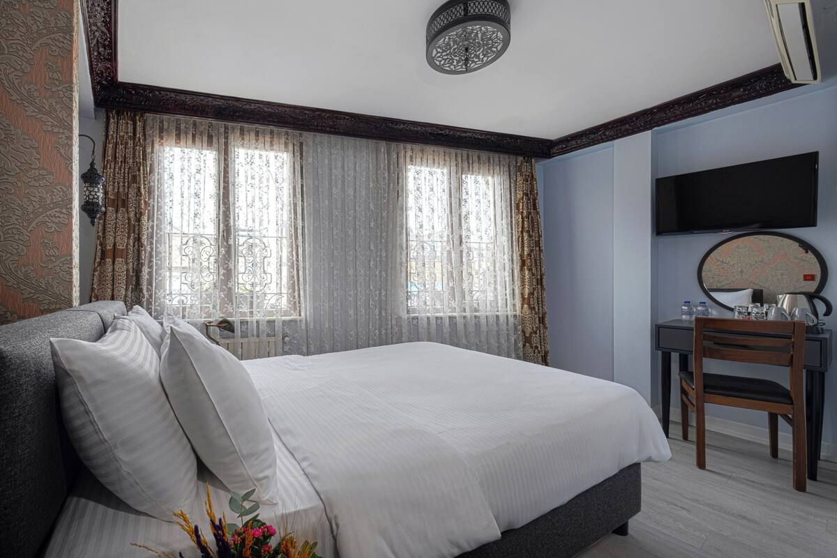 A hotel room with a large bed, a desk with a chair, a TV, and a window with curtains.