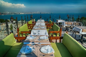 A dining area with tables set for two, overlooking a coastal cityscape. - Mytra Hotel (Istanbul)