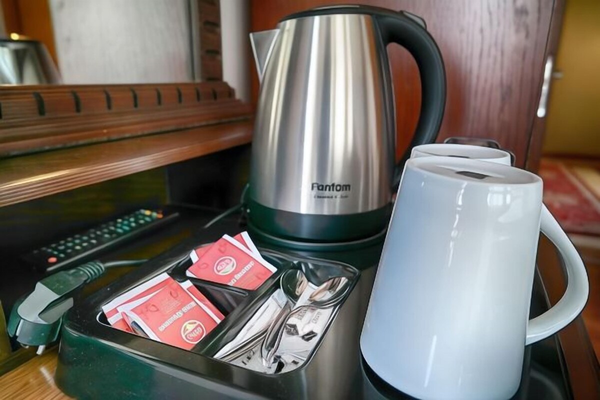 A tray with a stainless steel kettle, a white mug, and a compartment with a remote control and red cards.