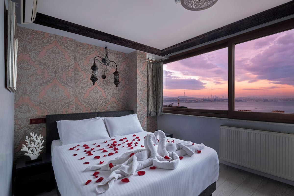 A hotel room with a large bed, a view of a city skyline at sunset, and a decorative wall.